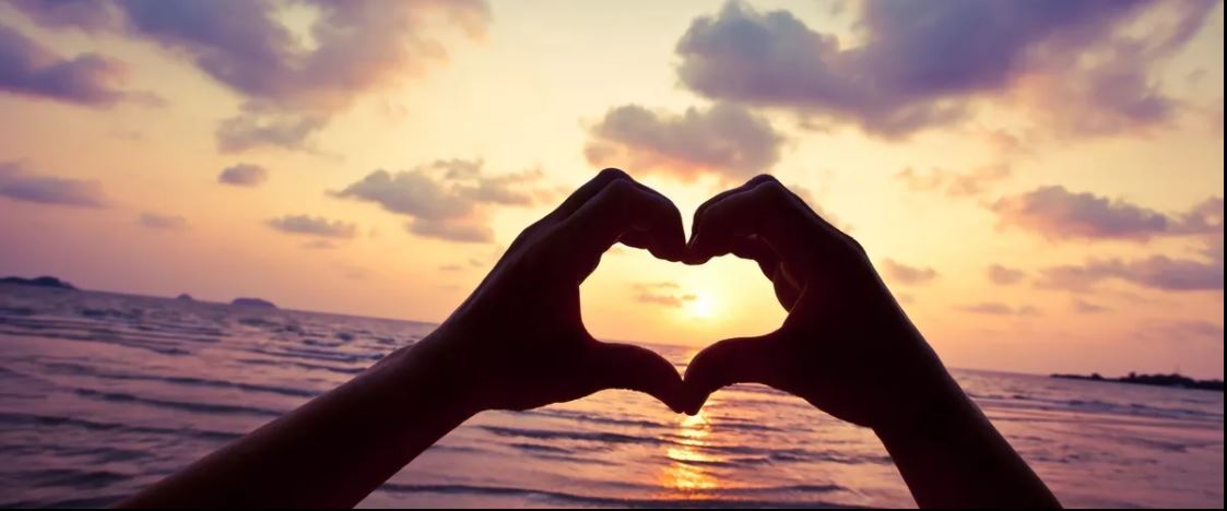 Fingers forming a heart with sunset in background