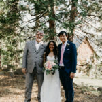 A photo of The officiant with the couple standing under a cedar tree after the wedding