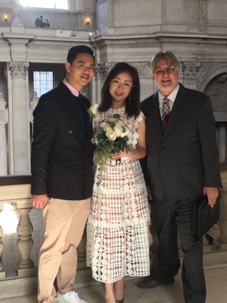 A photo of the Officiant posing with the couple on the third-floor balcony at San Francisco City Hall